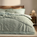 Hebden Percale Cotton Bedspread in Bay Green with quilted grid stitching, layered on a bed with striped pillowcases in a bedroom setting with a wooden headboard.