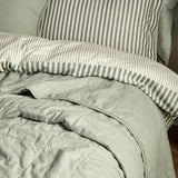 Hebden Percale Cotton Bedspread in Bay Green, quilted cotton throw folded on a bed with green and cream striped duvet cover and pillow.