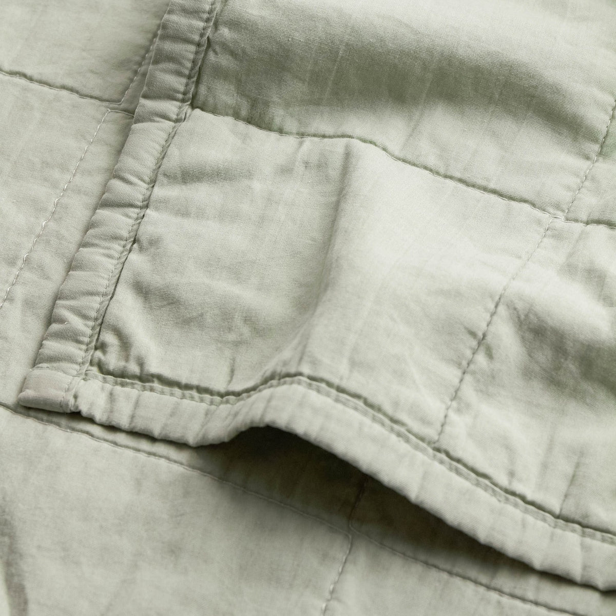 Close-up of the Hebden Percale Cotton Bedspread in Bay Green, showing a stitched panel seam and pocket detail on soft, garment-washed cotton fabric.