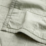 Close-up of the Hebden Percale Cotton Bedspread in Bay Green, showing a stitched panel seam and pocket detail on soft, garment-washed cotton fabric.