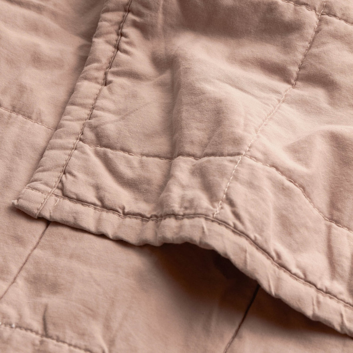 Close-up of the Hebden Percale Cotton Bedspread in Cotta, showing quilted cotton grid stitching and a folded corner edge in warm pink.
