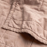 Close-up of the Hebden Percale Cotton Bedspread in Cotta, showing quilted cotton grid stitching and a folded corner edge in warm pink.