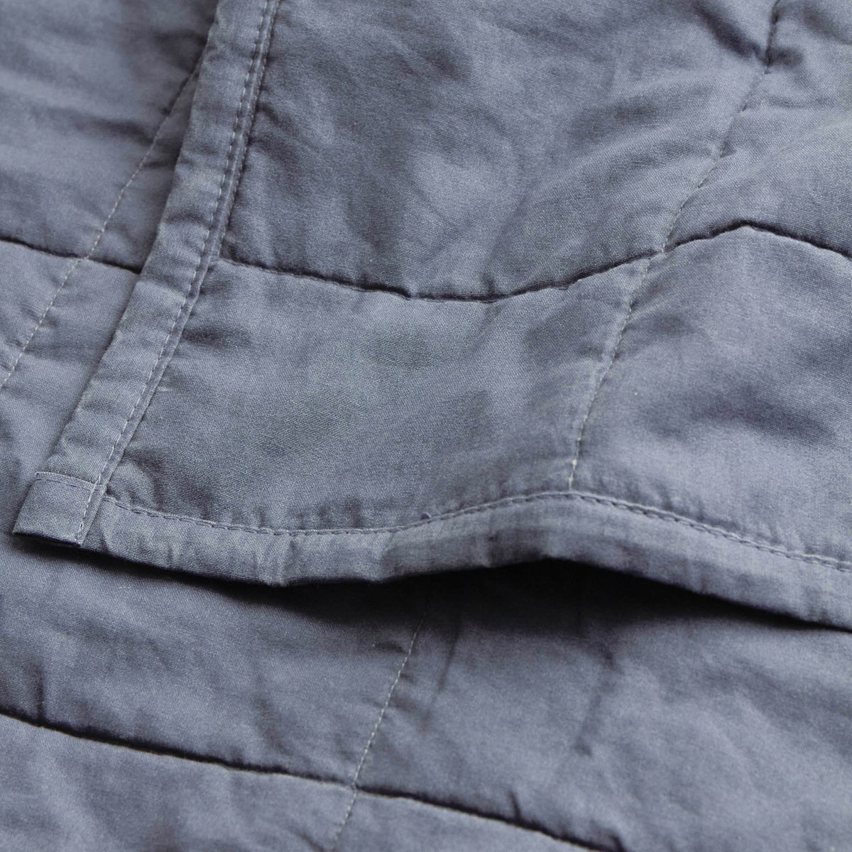 Close-up of the Hebden Percale Cotton Bedspread in denim blue, showing quilted grid stitching and a soft, garment-washed cotton texture with a folded pocket detail.