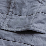 Close-up of the Hebden Percale Cotton Bedspread in denim blue, showing quilted grid stitching and a soft, garment-washed cotton texture with a folded pocket detail.