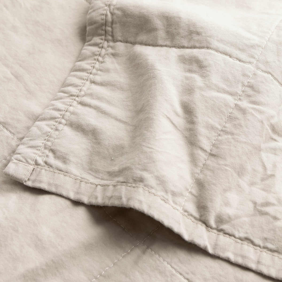 Close-up of the Hebden Percale Cotton Bedspread in stone, showing garment-washed cotton fabric with a softly crumpled texture and neat corner stitching.