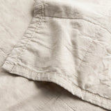Close-up of the Hebden Percale Cotton Bedspread in stone, showing garment-washed cotton fabric with a softly crumpled texture and neat corner stitching.