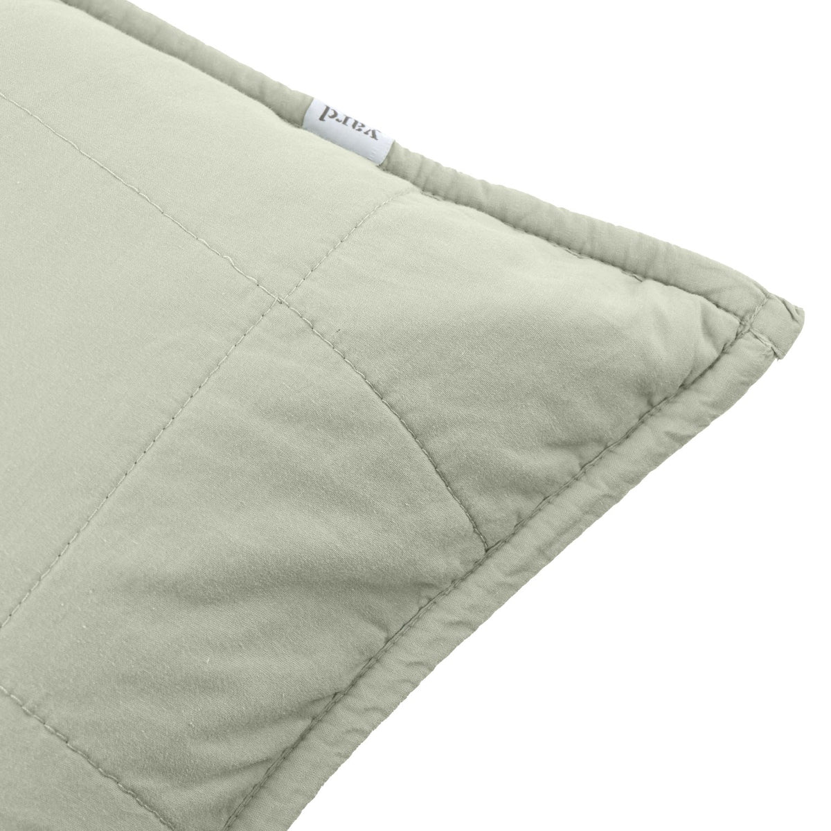 Close-up of the Hebden Percale Cotton Cushion in Bay Green, showing quilted grid stitching on soft sage cotton with a fabric brand label at the seam.