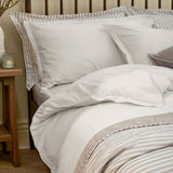 Hebden Cotton Plain Duvet Cover Set in chalk white on a bed with striped pillowcases and headboard, styled in a bedroom with a wooden side table.