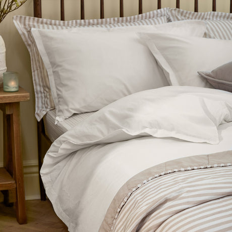 Hebden Cotton Plain Duvet Cover Set in chalk white on a bed with striped pillowcases and headboard, styled in a bedroom with a wooden side table.