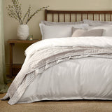 Hebden Cotton Plain Duvet Cover Set in chalk white on a bed with striped pillowcases and a quilted throw, wooden headboard and nightstand in a bedroom setting.