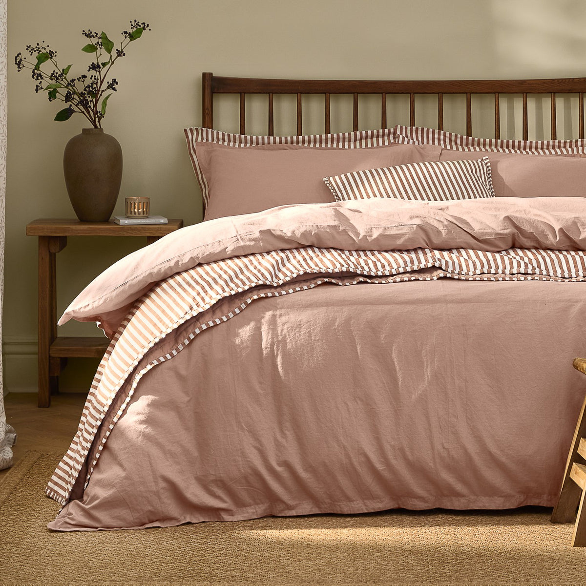 Hebden Cotton Plain Duvet Cover Set in Cotta dusky pink on a bed with wooden spindle headboard, showing striped reverse and pillowcases in tan and cream.