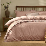 Hebden Cotton Plain Duvet Cover Set in Cotta dusky pink on a bed with wooden spindle headboard, showing striped reverse and pillowcases in tan and cream.
