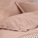 Close-up of the Hebden Cotton Plain Duvet Cover Set in Cotta, showing dusky pink washed cotton with a tan and cream striped reverse peeking through the folds.