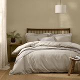 Hebden Cotton Plain Duvet Cover Set in Stone dressing a wooden slatted bed with striped accent pillows in a warm beige bedroom.