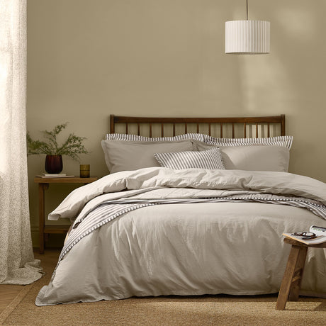 Hebden Cotton Plain Duvet Cover Set in Stone dressing a wooden slatted bed with striped accent pillows in a warm beige bedroom.
