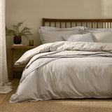 Hebden Cotton Plain Duvet Cover Set in Stone on a wooden spindle bed, styled with striped cushions in a bedroom setting.