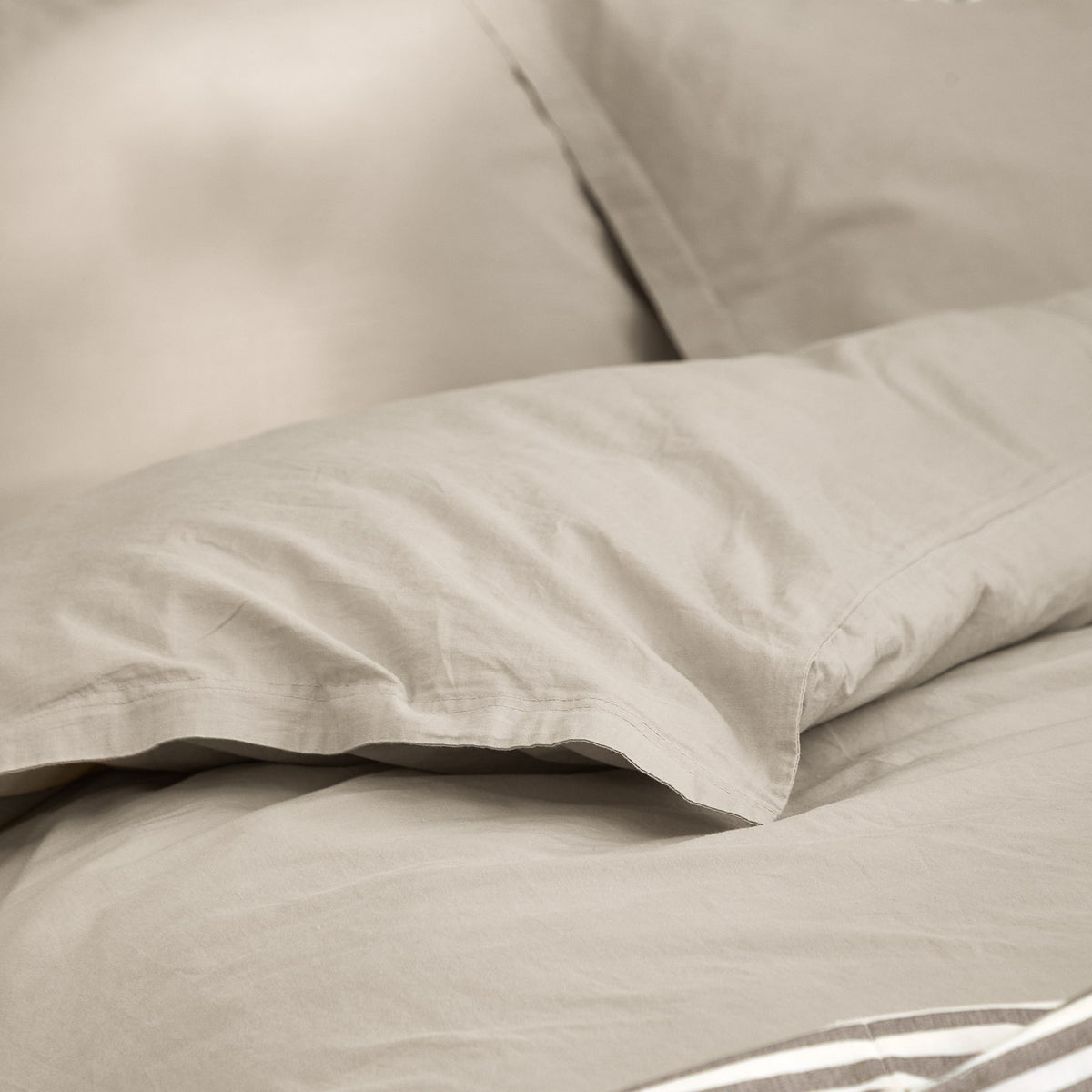 Close-up of the Hebden Cotton Plain Duvet Cover Set in Stone, showing washed cotton fabric in a soft grey-beige tone with a folded pillowcase edge.