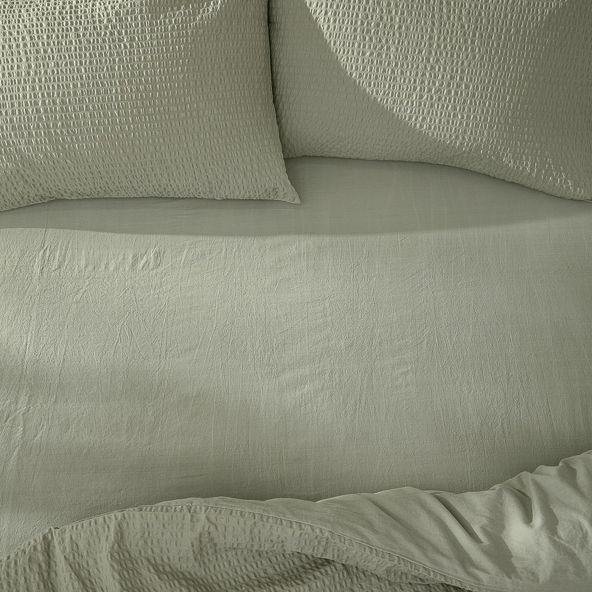 Hebden Percale Cotton Fitted Sheet in Bay Green on a bed, with matching textured pillowcases and a softly crinkled cotton percale surface.