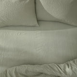 Hebden Percale Cotton Fitted Sheet in Bay Green on a bed, with matching textured pillowcases and a softly crinkled cotton percale surface.