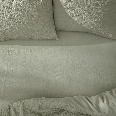 Hebden Percale Cotton Fitted Sheet in Bay Green on a bed, with matching textured pillowcases and a softly crinkled cotton percale surface.