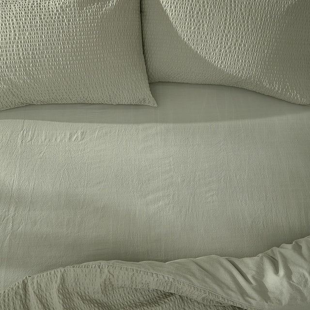 Hebden Percale Cotton Fitted Sheet in Bay Green on a bed, with matching textured pillowcases and a softly crinkled cotton percale surface.