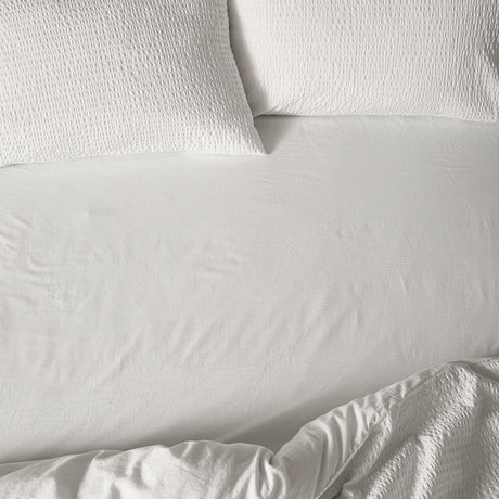 Hebden Percale Cotton Fitted Sheet in Chalk, a soft off-white 100% cotton bedsheet with a crinkled matt texture, shown fitted on a bed with matching waffle-textured pillowcases.