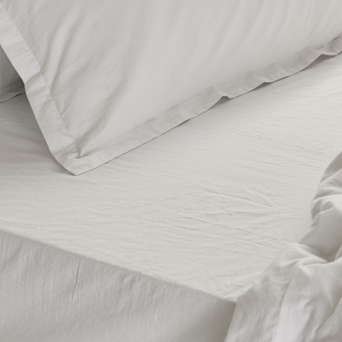 Close-up of the Hebden Percale Cotton Fitted Sheet in Chalk on a bed, showing crisp white cotton with a gently crinkled texture alongside matching pillow shams.