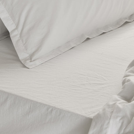 Close-up of the Hebden Percale Cotton Fitted Sheet in Chalk on a bed, showing crisp white cotton with a gently crinkled texture alongside matching pillow shams.