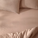 Hebden Percale Cotton Fitted Sheet in Cotta pink, shown on a bed with waffle-textured pillows and a matching quilted cover in soft natural light.