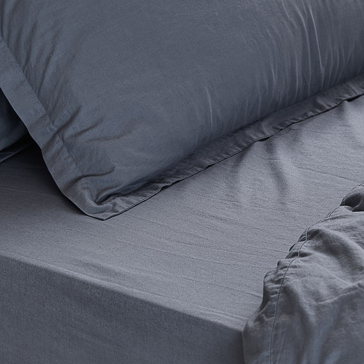 Close-up of the Hebden Percale Cotton Fitted Sheet in denim blue on a mattress, with a matching pillowcase showing the soft, textured cotton weave.