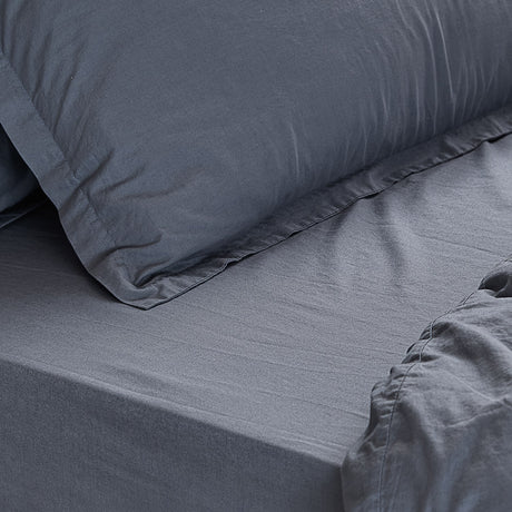 Close-up of the Hebden Percale Cotton Fitted Sheet in denim blue on a mattress, with a matching pillowcase showing the soft, textured cotton weave.