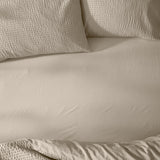 Hebden Percale Cotton Fitted Sheet in stone, shown smoothly fitted on a bed with matching waffle-textured pillowcases in the same warm beige tone.