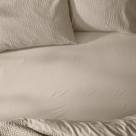 Hebden Percale Cotton Fitted Sheet in stone, shown smoothly fitted on a bed with matching waffle-textured pillowcases in the same warm beige tone.