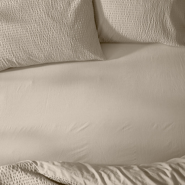 Hebden Percale Cotton Fitted Sheet in stone, shown smoothly fitted on a bed with matching waffle-textured pillowcases in the same warm beige tone.
