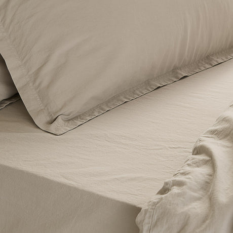 Close-up of the Hebden Percale Cotton Fitted Sheet in stone, showing the elasticated corner, matt cotton weave, and a matching pillowcase on the bed.