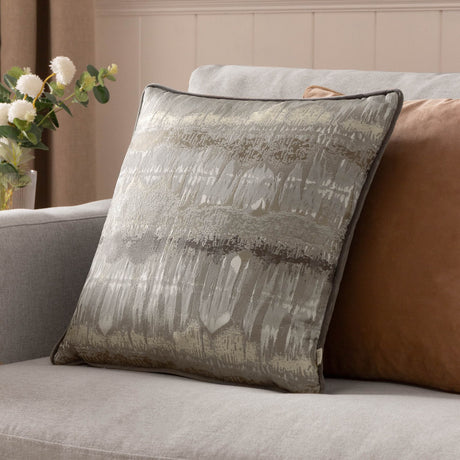 Inca Jacquard Velvet Cushion in Steel Grey with abstract metallic gold and silver textured pattern, piped edge, shown on a living room sofa.