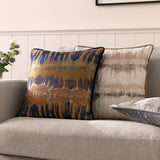 Inca Jacquard Velvet Cushion in steel grey with metallic gold-brown abstract pattern, shown on a sofa beside a matching navy and gold patterned cushion.