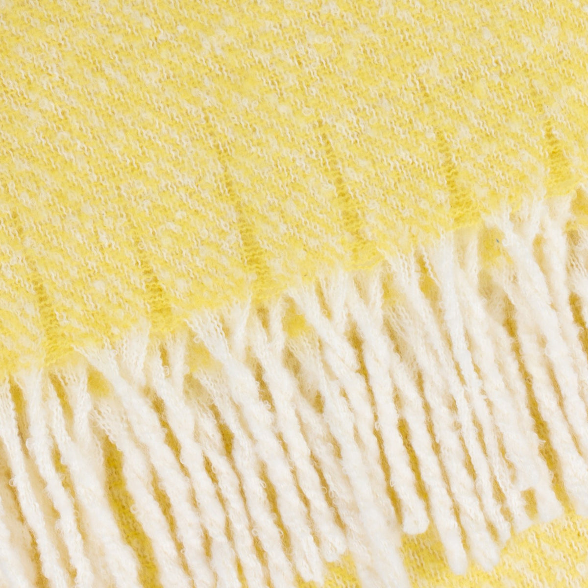 Close-up of the Isla Plain Polyester Throw in butter yellow, showing woven cream-flecked texture and knotted tassel fringe along the edge.