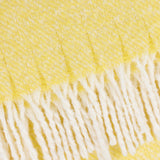 Close-up of the Isla Plain Polyester Throw in butter yellow, showing woven cream-flecked texture and knotted tassel fringe along the edge.