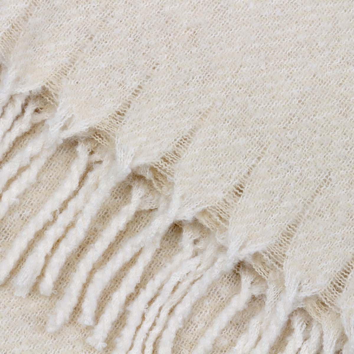 Close-up of the Isla Plain Polyester Throw in cream, showing its open woven texture and knotted tassel fringe edge.