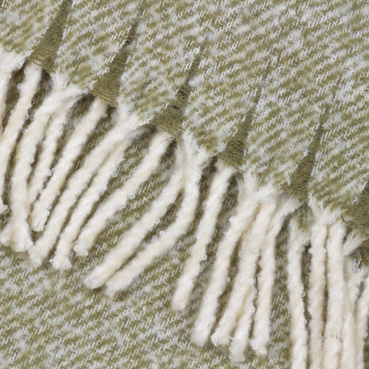 Close-up of the Isla Plain Polyester Throw in sage green, showing a woven herringbone texture edged with cream tasselled fringing.