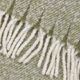 Close-up of the Isla Plain Polyester Throw in sage green, showing a woven herringbone texture edged with cream tasselled fringing.