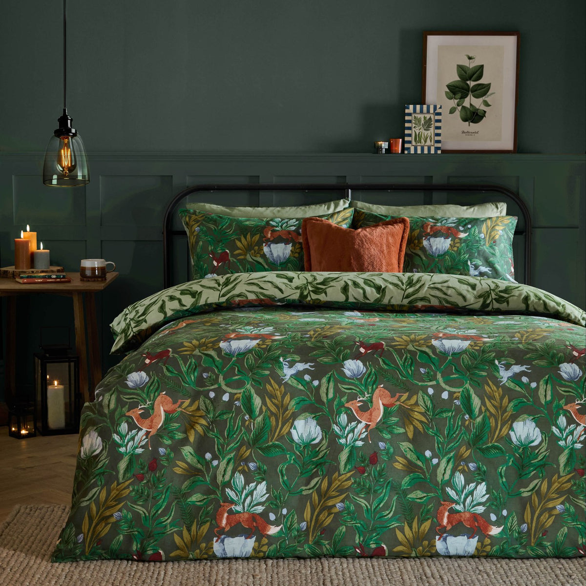 Into The Woods reversible duvet cover set in forest green, styled on a bed with woodland fox and floral print, paired with sage leaf-pattern pillowcases and rust cushions.