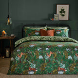 Into The Woods reversible duvet cover set in forest green, styled on a bed with woodland fox and floral print, paired with sage leaf-pattern pillowcases and rust cushions.