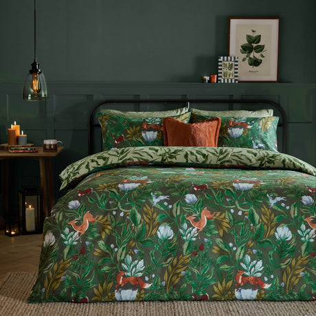 Into The Woods reversible duvet cover set in forest green, styled on a bed with woodland fox and floral print, paired with sage leaf-pattern pillowcases and rust cushions.