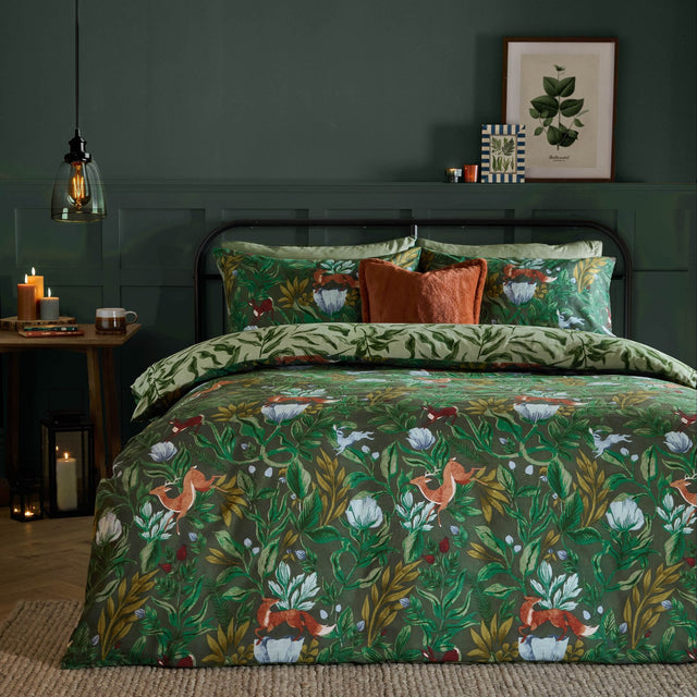 Into The Woods reversible duvet cover set in forest green, styled on a bed with woodland fox and floral print, paired with sage leaf-pattern pillowcases and rust cushions.