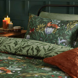 Forest green Into The Woods reversible duvet set with woodland-print pillowcase featuring foxes, hares and foliage, styled on a bed with rust cushions in a dark green bedroom.