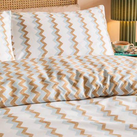 Izzie Reversible Striped Duvet Cover Set in blue and caramel zig-zag pattern, shown on a bed with matching pillowcases in a bedroom setting.