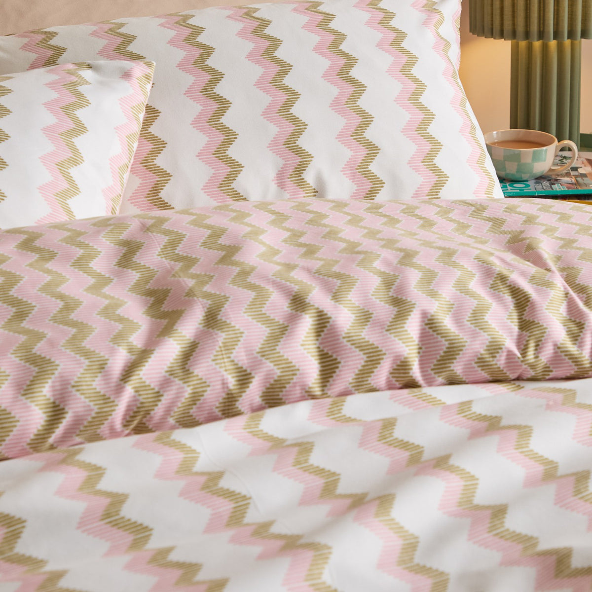 Izzie Reversible Duvet Cover Set in pink and olive-green zig-zag stripes on white, shown on a bedroom bed with matching pillowcases.