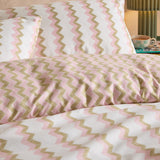 Izzie Reversible Duvet Cover Set in pink and olive-green zig-zag stripes on white, shown on a bedroom bed with matching pillowcases.